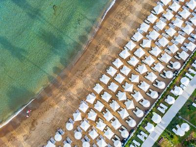 Strand mit Reihen weißer Sonnenschirme und Liegen am klaren, türkisfarbenen Meer.