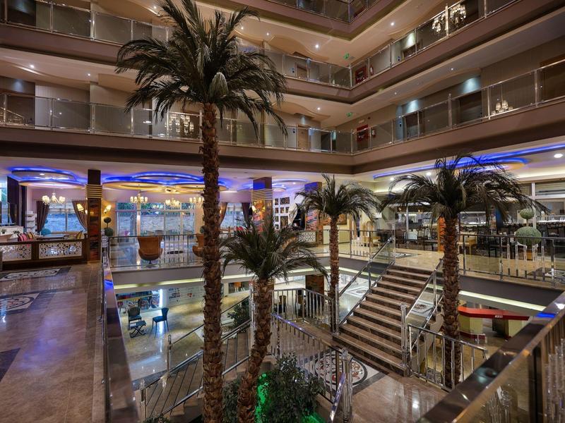 Innenraum eines modernen Einkaufszentrums mit Palmen, Treppen und mehrstöckigen Glasgeländern.