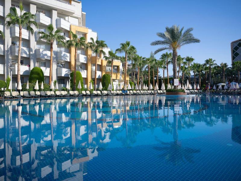 Großer blauer Pool mit Palmen und Hotelgebäude unter klarem blauem Himmel.