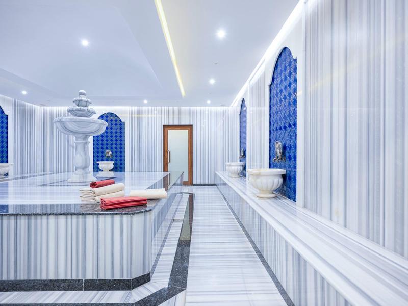 Eleganter Dampfbadraum mit Marmor, blauen Nischen und Wasserbrunnen, modern beleuchtet.