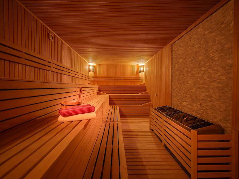 Innenraum einer Holzsauna mit mehrstufigen Sitzbänken und warmem Licht, zwei roten Handtüchern liegen.