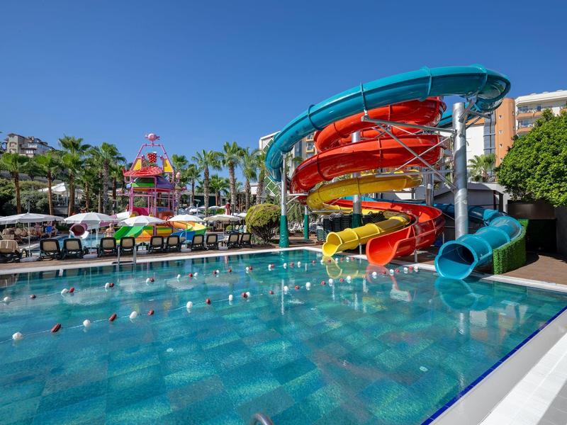 Großer Swimmingpool mit bunten Wasserrutschen und Palmen bei sonnigem Himmel.