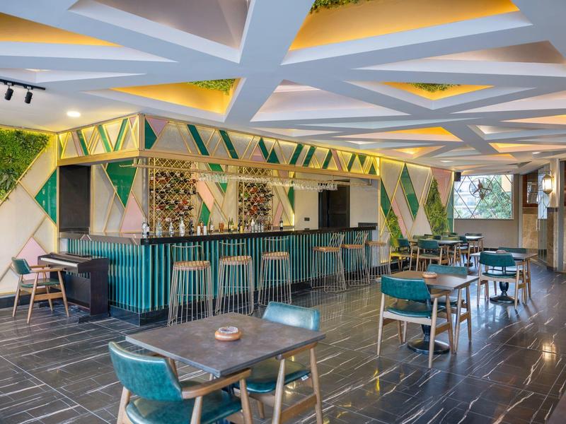 Modernes Café mit grünen Stühlen, Holztischen und einer Bar mit dekorativem Fliesenmuster.