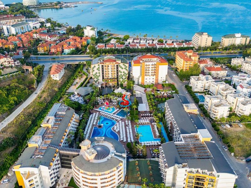 Luftaufnahme eines großen Hotels mit Pool, umgeben von Straßen, Wohnungen und Meer im Hintergrund.