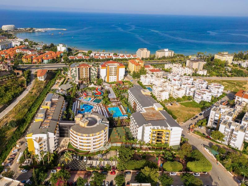 Küstenstadt mit modernen Wohngebäuden, Pools und grünem Umfeld am blauen Meer unter klarem Himmel.