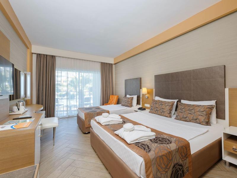 Ein modernes Hotelzimmer mit zwei Betten, hellen Holzmöbeln und Balkon mit Tageslicht.