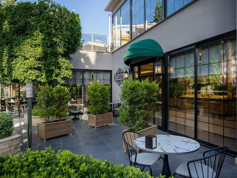 Moderner Gastraum mit schwarzem Boden, großen Fenstern, grünen Pflanzen und rundem Marmor-Tisch.