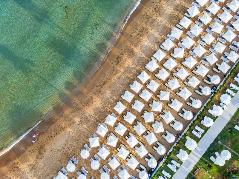 Strand mit Reihen weißer Sonnenschirme und Liegen am klaren, türkisfarbenen Meer.