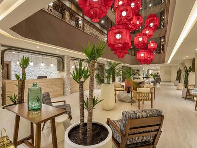 Área de vestíbulo de hotel moderna con lámparas rojas colgantes, plantas y asientos cómodos.