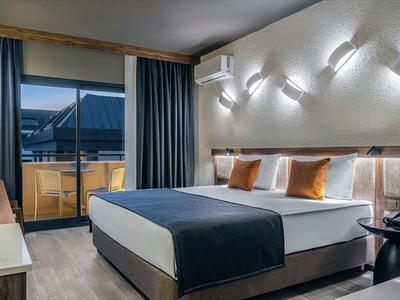 Habitación de hotel moderna con cama doble, balcón e iluminación elegante al anochecer.