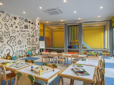 Sala de juegos y manualidades infantil luminosa y colorida con mesas, sillas y ventanales.