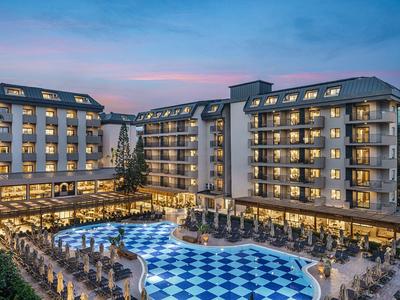 Večerní pohled na osvětlený hotel s modro-bílým bazénem a okolními sezeními.