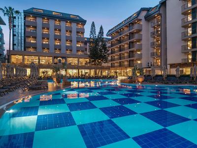 Večerní pohled na osvětlený hotel s velkým bazénem a palmami.
