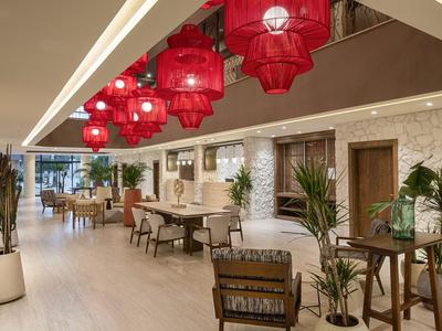 Moderní hotelová lobby s červenými lucernami, dřevěným nábytkem a rostlinami na světlé podlaze.