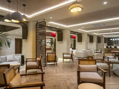 Moderní hotelová lounge s dřevěnými židlemi, rostlinami a teplým osvětlením.