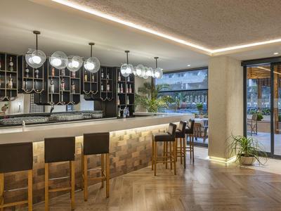 Moderní hotelový bar s dřevěným pultem, černými barovými židlemi a stylovými globusovými světly.