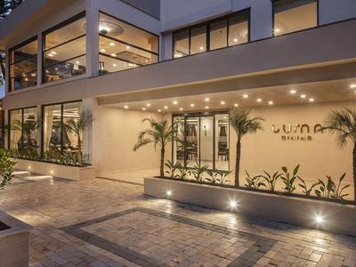 Moderní hotel se osvětleným vchodem, rostlinami a velkými okny za soumraku.