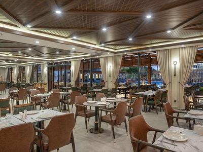 Prostorná restaurace s moderním dřevěným nábytkem a velkými okny s výhledem na venkovní prostor.