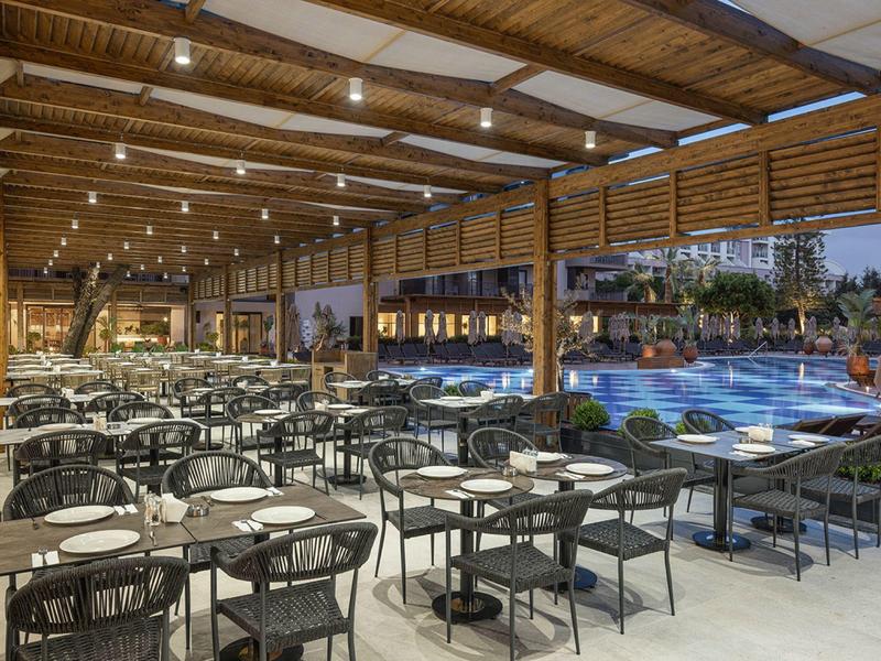 Gran restaurante cubierto con sillas negras y vista a la piscina iluminada por la noche