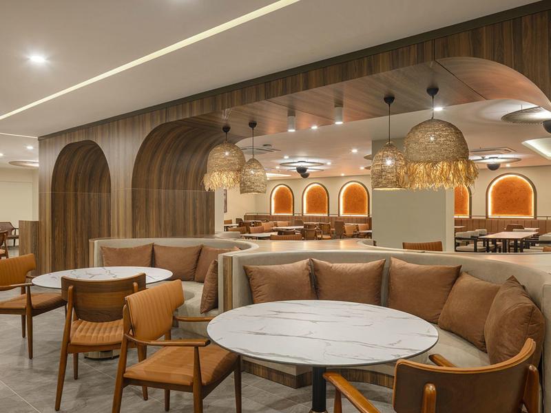 Área de restaurante de hotel moderno con sillones de cuero marrón, mesas redondas y luces decorativas.