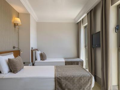 Moderní hotelový pokoj se dvěma jednolůžky, neutrálními tóny a okny s závěsy.