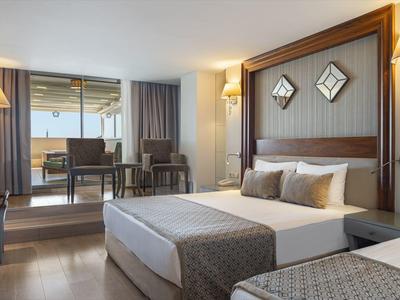 Moderně zařízený hotelový pokoj se dvěma postelemi, stolem a velkým oknem s výhledem ven.