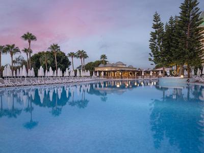 Ampia piscina con lettini e palme al tramonto in un resort.