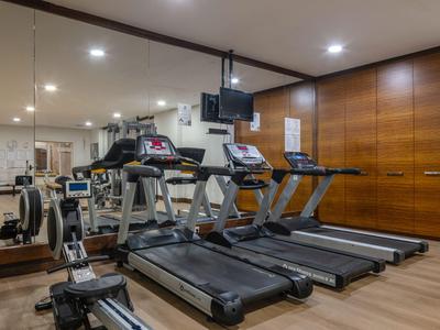Sala fitness con tapis roulant, vogatori e pannelli in legno sulla parete.