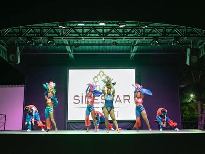 Otto ballerini in costumi colorati si esibiscono su un palco all'aperto illuminato.