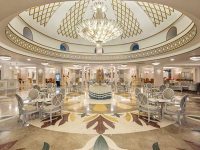 Elegante area lounge dell'hotel con lampadario, tavoli rotondi e sedie ornate sotto una cupola.