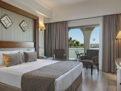 Světý hotelový pokoj s manželskou postelí, nočními stolky, posezením a výhledem na terasu se zahradou.