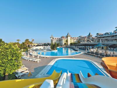 View of a large hotel pool with water slides and multiple lounge areas under a blue sky.