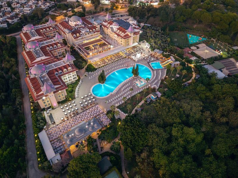 Letecký pohled na velké letovisko s zakřiveným bazénem obklopeným lesem.