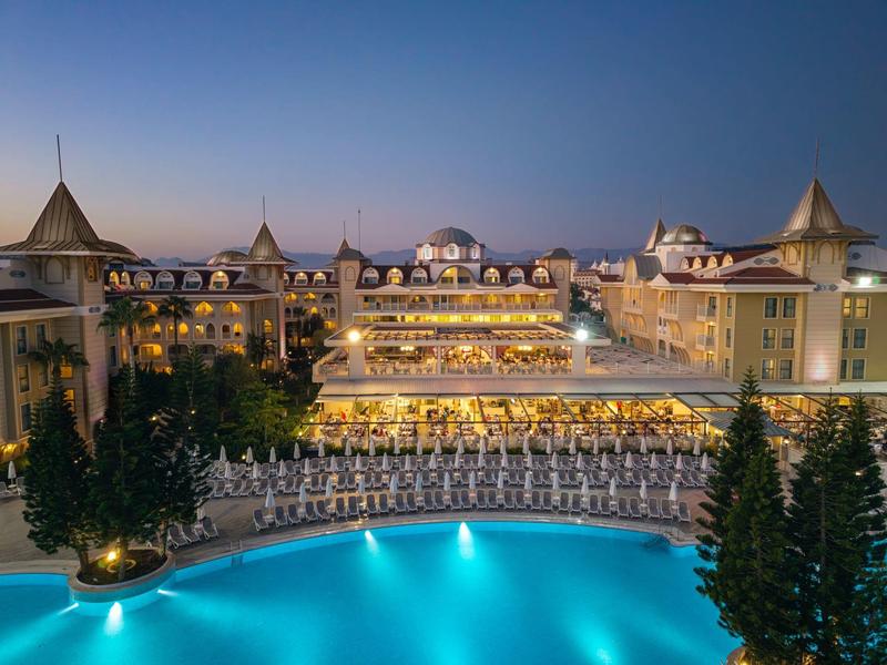 Osvětlený hotel s bazénem a mnoha lehátky za soumraku