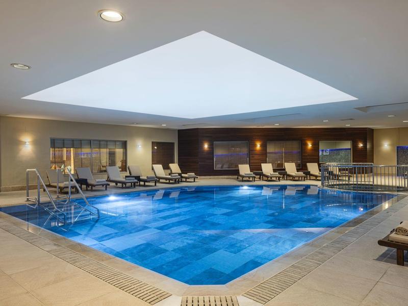 Vnitřní bazén s modrými dlaždicemi a lehátky v moderní hotelové oblasti