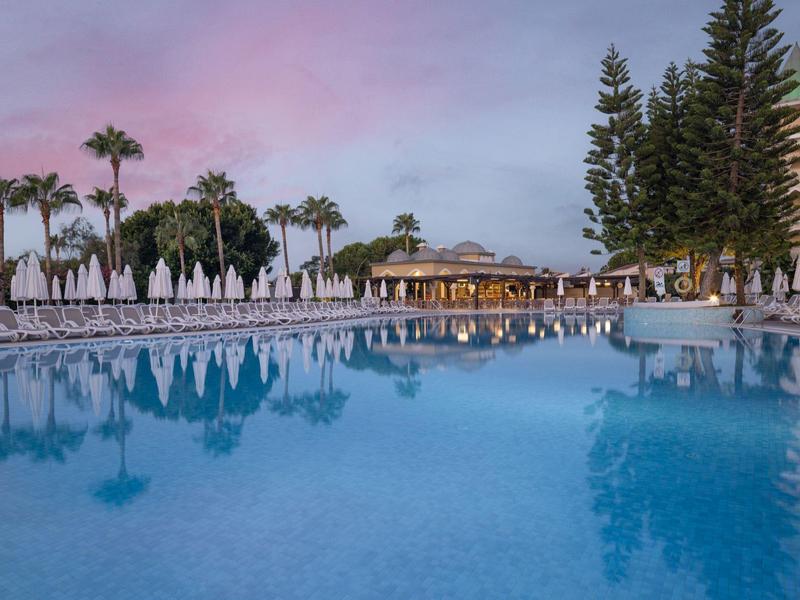 Velký bazén s lehátky a palmami při západu slunce v resortu.