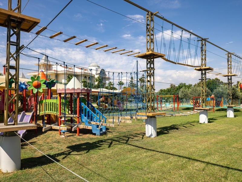 Lanový park a hřiště vedle hotelu s zeleným trávníkem a modrou oblohou.