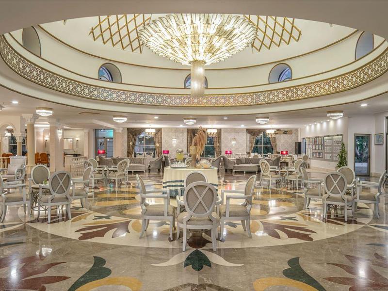 Prostorná hotelová hala s elegantními křesly, mramorovou podlahou a lustry pod kopulovým stropem.