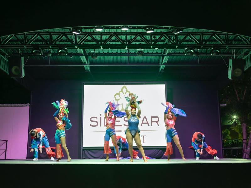 Představení na jevišti s několika tanečníky v pestrobarevných kostýmech v noci