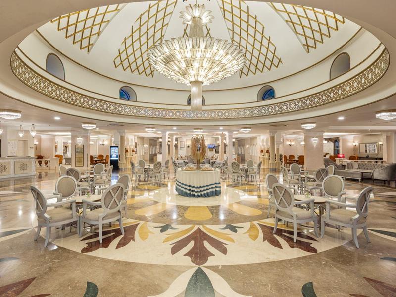 Luxusní hotelová lobby s ozdobným lustrem, elegantními posezeními a dekorativním vzorem na podlaze.