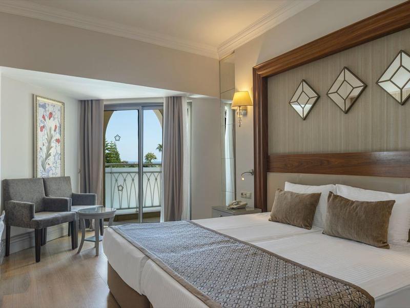 Elegantní hotelový pokoj s velkou postelí, posezením a balkonem s výhledem na moře.