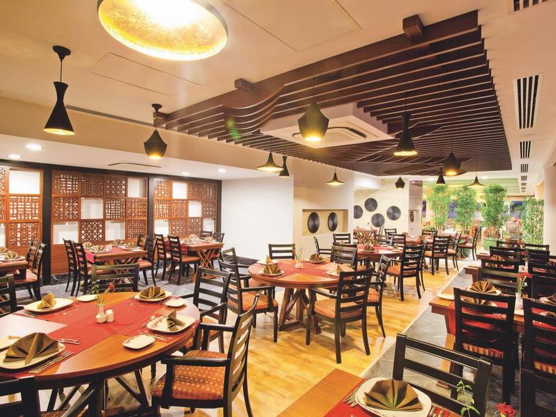 Prostorná jídelna s dřevěnými stoly a židlemi, elegantním osvětlením a dekorativními prvky.