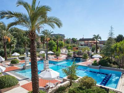 Hotel-Außenpool mit Palmen, Sonnenschirmen und Liegestühlen unter blauem Himmel.