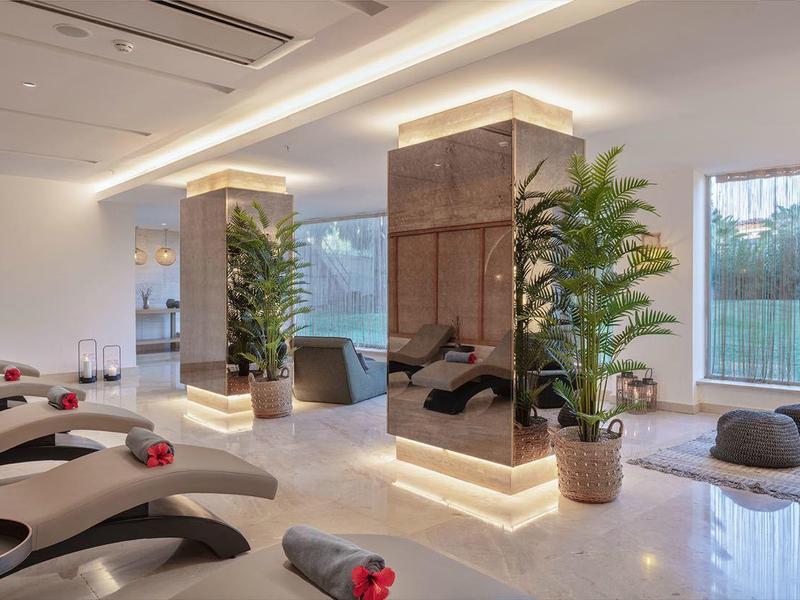 Area benessere moderna con lettini, piante e grande finestra con vista sull'esterno.