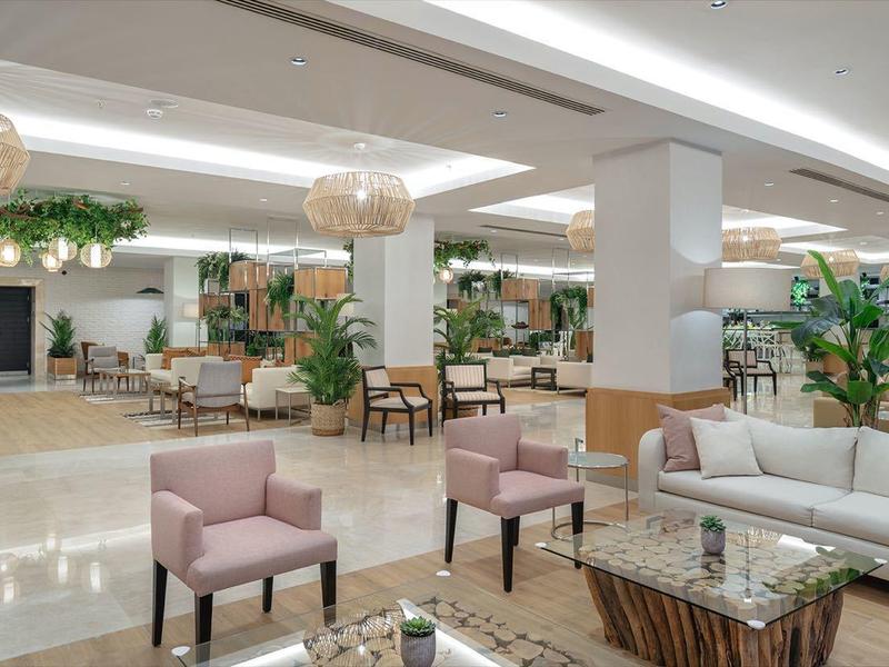 Moderna hall d'hotel con aree salotto confortevoli, piante verdi e ambiente luminoso.