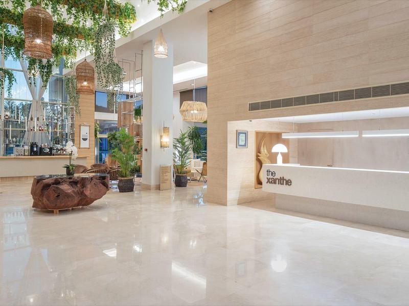 Ampia hall dell'hotel con pavimento in marmo chiaro, reception e piante rigogliose.