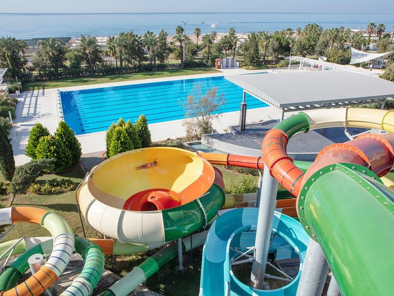 Vista di un parco acquatico con scivoli, piscina e mare sullo sfondo.