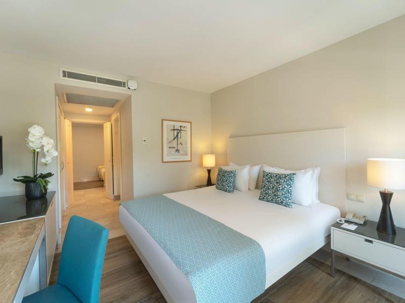 Camera d'hotel luminosa con letto matrimoniale, due comodini, sedia e TV a schermo piatto.