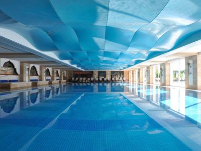 Großes Schwimmbecken mit blauer Wasserfläche und blauem Stoffdach im Innenbereich.