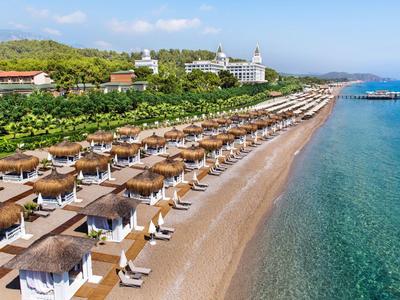 Strand mit Reihen von Sonnenschirmen und Liegestühlen, grüner Hang im Hintergrund, klares Meer Wasser.